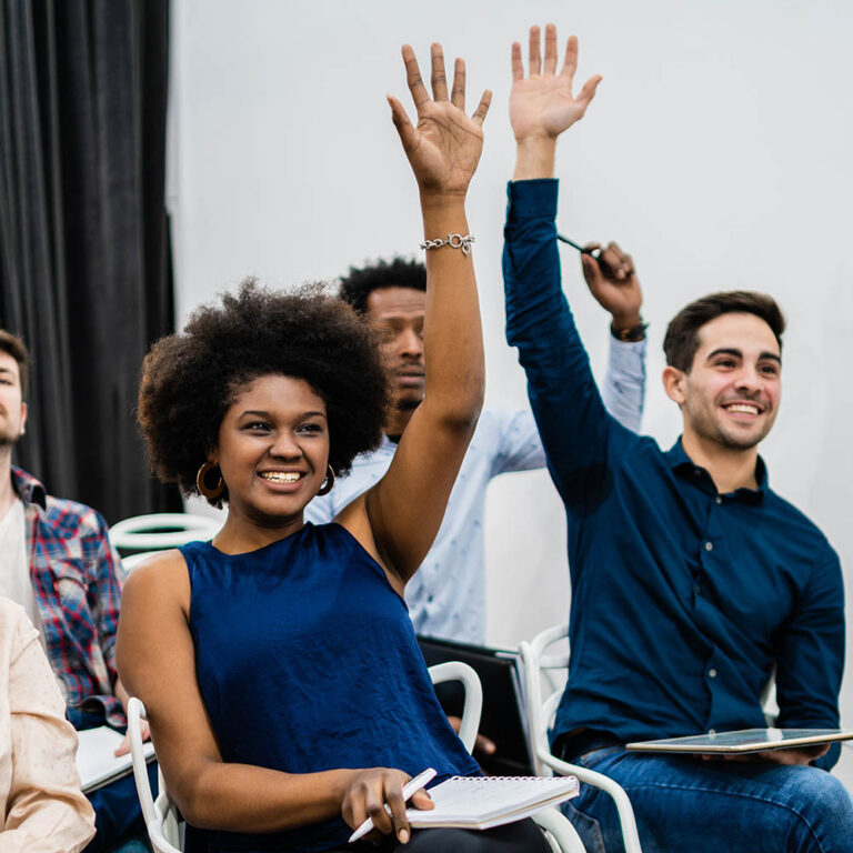 Group of young people sitting on conference together while raising their hands to ask a question. Business team meeting seminar training concept.